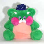 A green plush dragon-like teddy bear with a pink belly, pink cheeks, white eyes and nose, wearing a navy blue starry nightcap, photographed against a plain white background.